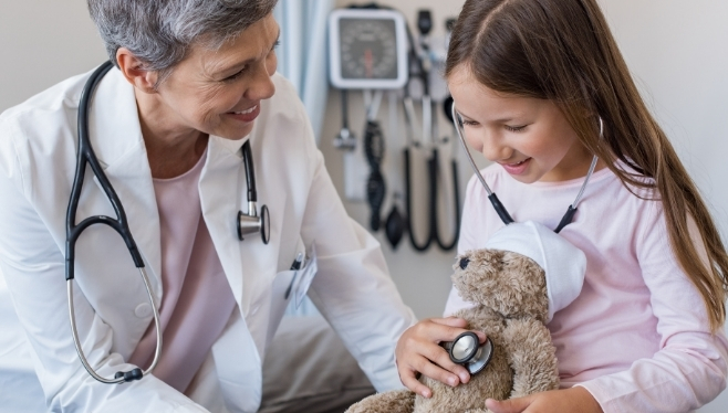 Older woman doctor checking a little girl's teddy bears' heartbeat | PRF Requirements | Provider Relief Funding | CARES Act | Business Consulting | COVID-19 Financial Updates